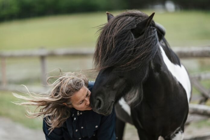En dame kysser en hest på mulen, i baggrunden kan man se noget eng og noget græs